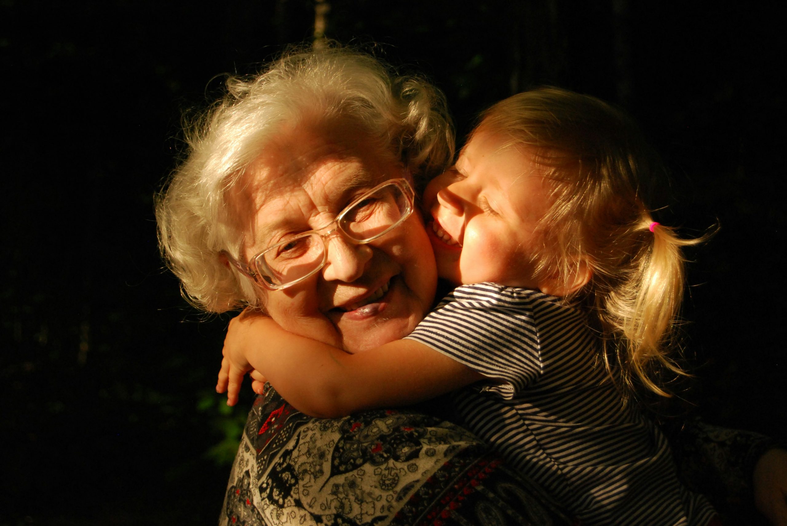 Elderly grandparent embracing smiling young grandchild in supportive hug, symbolizing a positive family and caregiver bond