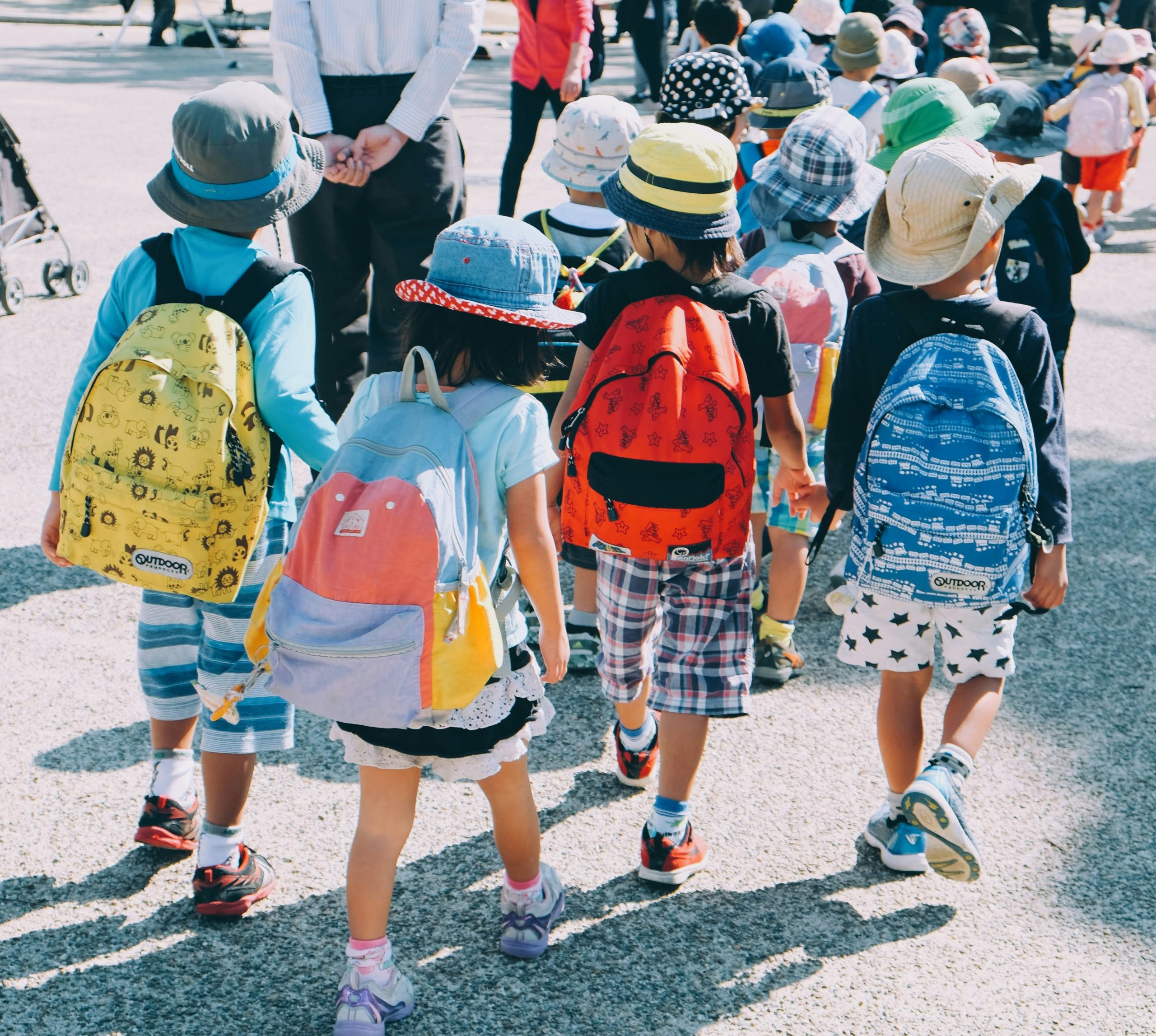 Young children ages 3 years old to 12 years old walking into to pre-school and elementary school carrying backpacks filled with support materials