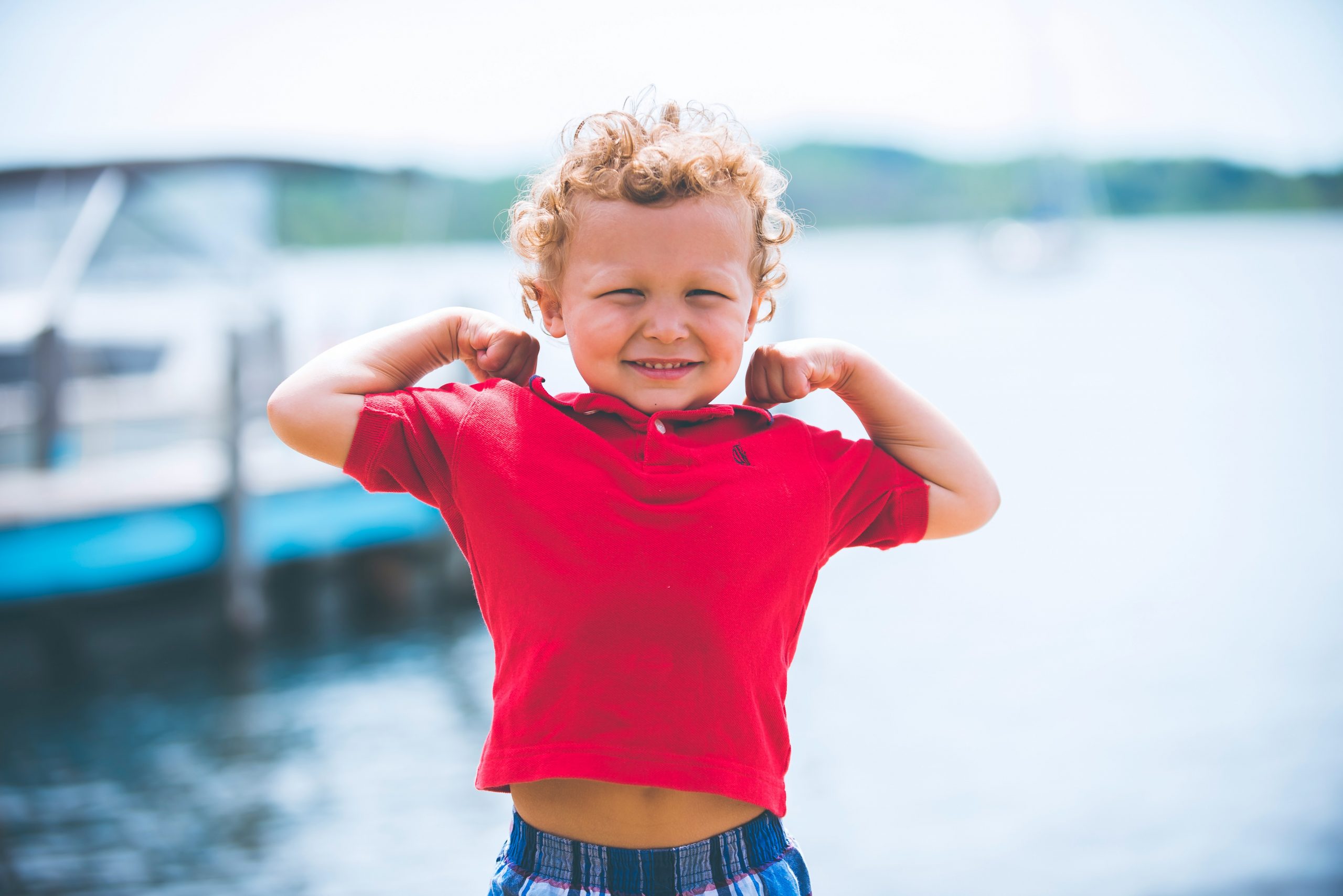 Young 4-year-old boy flexes muscles with a smile, symbolizing strength, health and growth