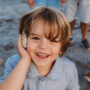 Young 5-year-old boy smiling and talking into seashell as if it is a phone