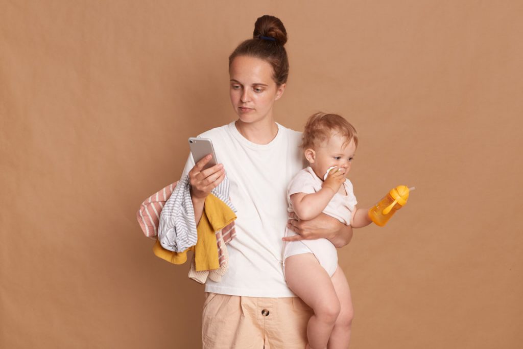 Young holding toddler daughter and using mobile phone to find parental resource apps